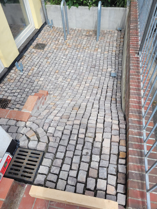 Frisch verlegte Natursteinpflasterfläche mit Stufen, Entwässerung und Gefälle in einem Eingangsbereich