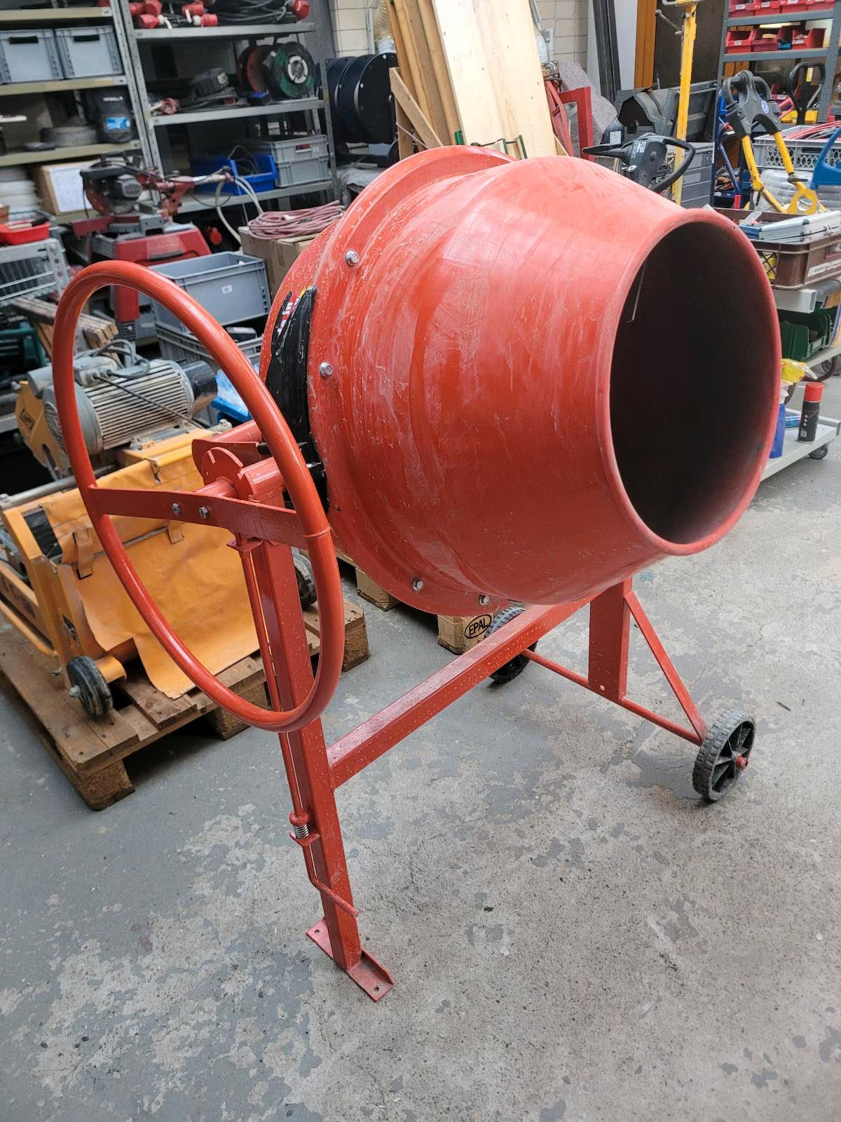 Leerer, orangener Betonmixer mit großem Rad zum mischen und Rädern auf einer Seite zum Schieben