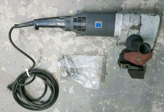 Ein schwarz-silberner Blechnager mit Kabel und seitlichem Handgriff, sowie eine durchsichtige Tüte mit weiteren Aufsätzen.