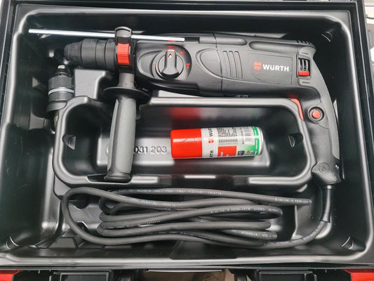Ein schwarz-roter Bohrhammer mit Kabel, Handgriff und Aufsatz in der Box.