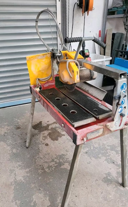 Ein rot-gelber Nass-Steinschneider. Mit vier Beinen, aufgebaut wie ein Tisch und mit einem Kreis-Sägeblatt.
