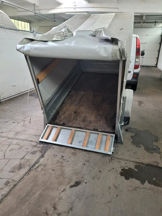 Ein Geschlossener Kippanhänger, hier im gekippten Zustand und hinten offen.