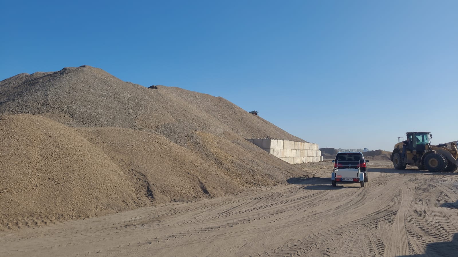 Ein Auto und ein Bagger vor einem großen Haufen Schüttgut
