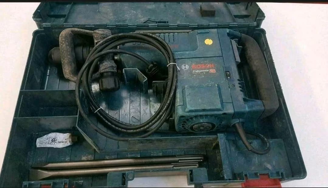 Türkis-schwarzer Stemmhammer in der Box mit Kabel und zwei großen Meißelaufsätzen.